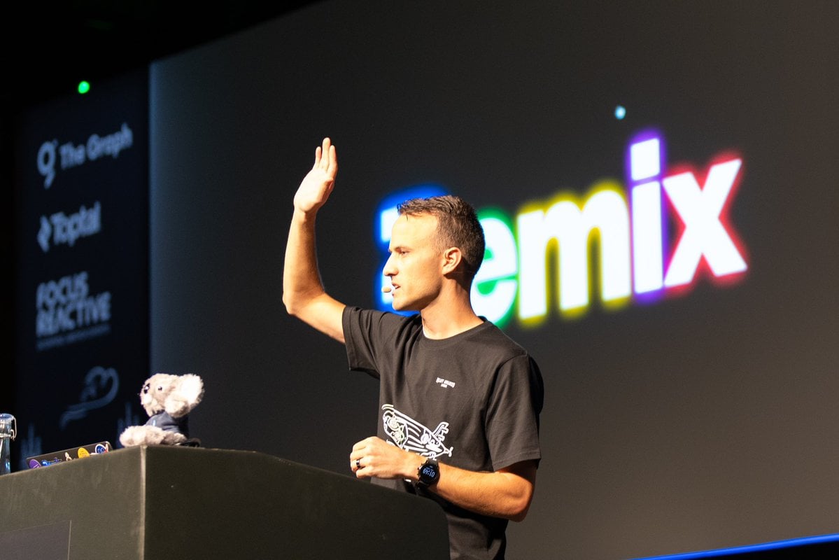Kent on stage raising his hand with the Remix logo behind him