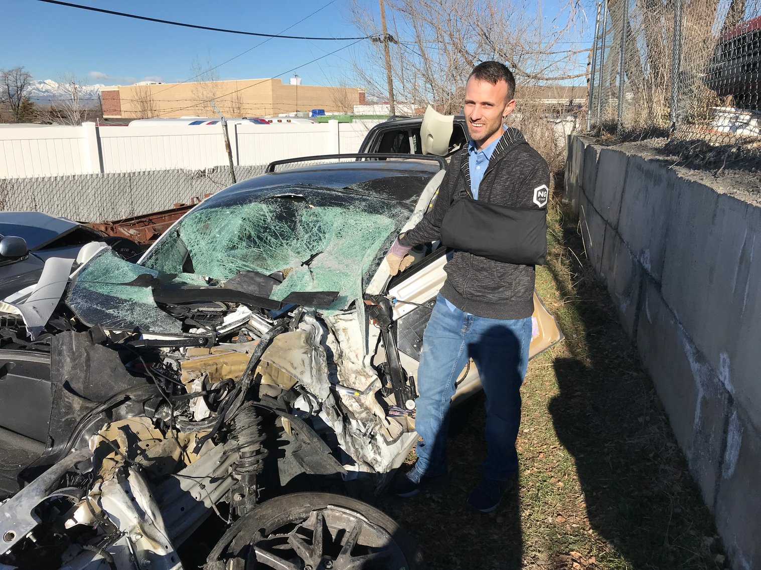 Kent standing by a wrecked Tesla model 3 in a junkyard. It's completely crushed.