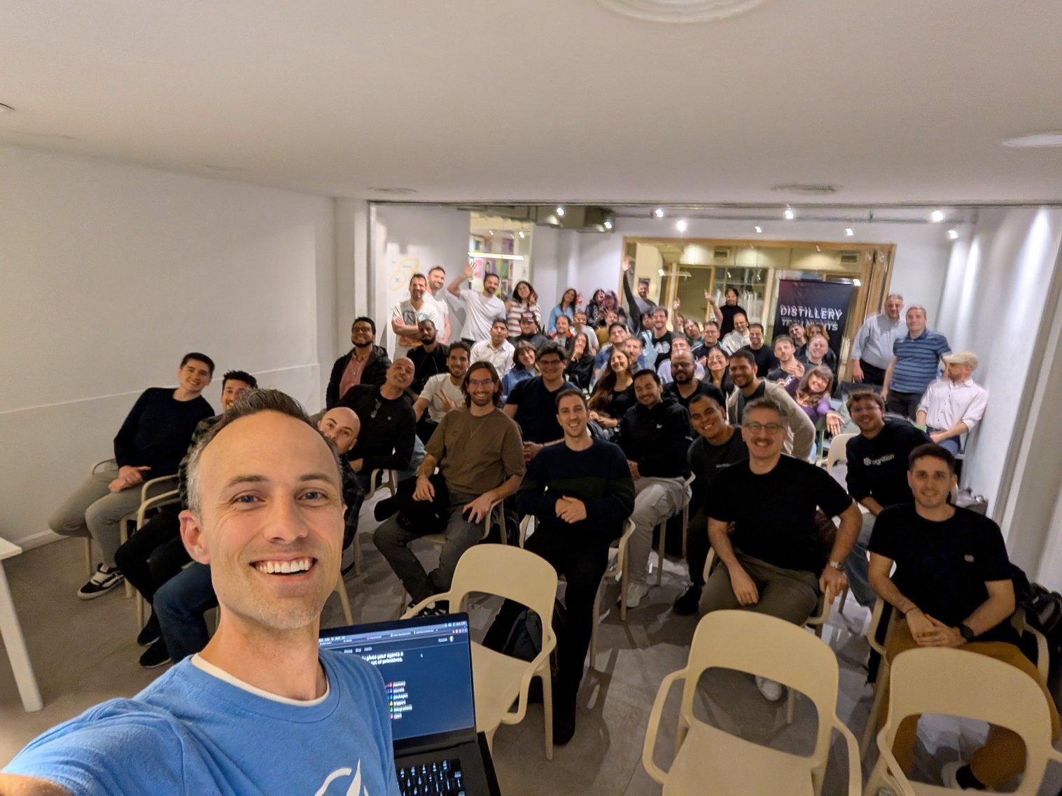 Kent C. Dodds taking a selfie in front of a room full of developers at a Distillery Tech Night in Buenos Aires, with a Distillery banner in the background