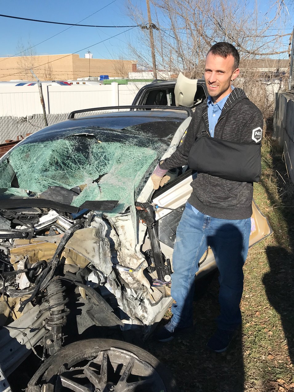 Kent standing by a wrecked Tesla model 3 in a junkyard. It's completely crushed.