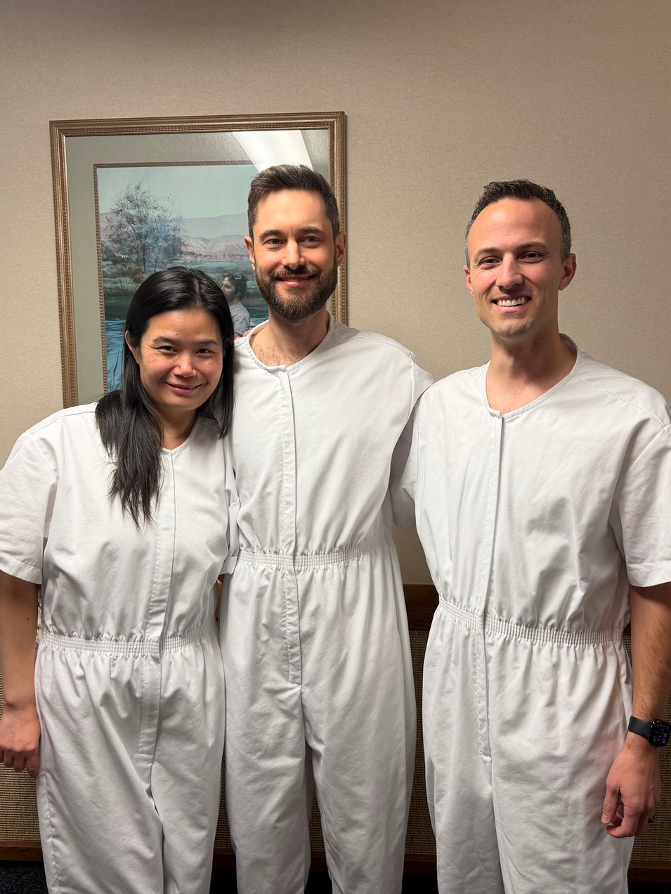 Beiyi, Jeremiah Dow, and Kent C. Dodds stand side by side in white baptismal clothing, smiling indoors at a church.