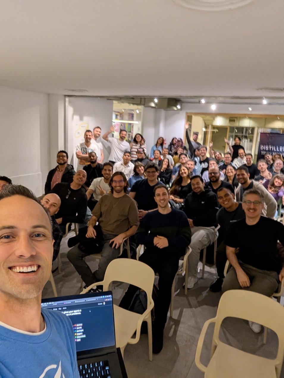 Kent C. Dodds taking a selfie in front of a room full of developers at a Distillery Tech Night in Buenos Aires, with a Distillery banner in the background