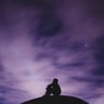 person sitting on black surface looking to a purple sky